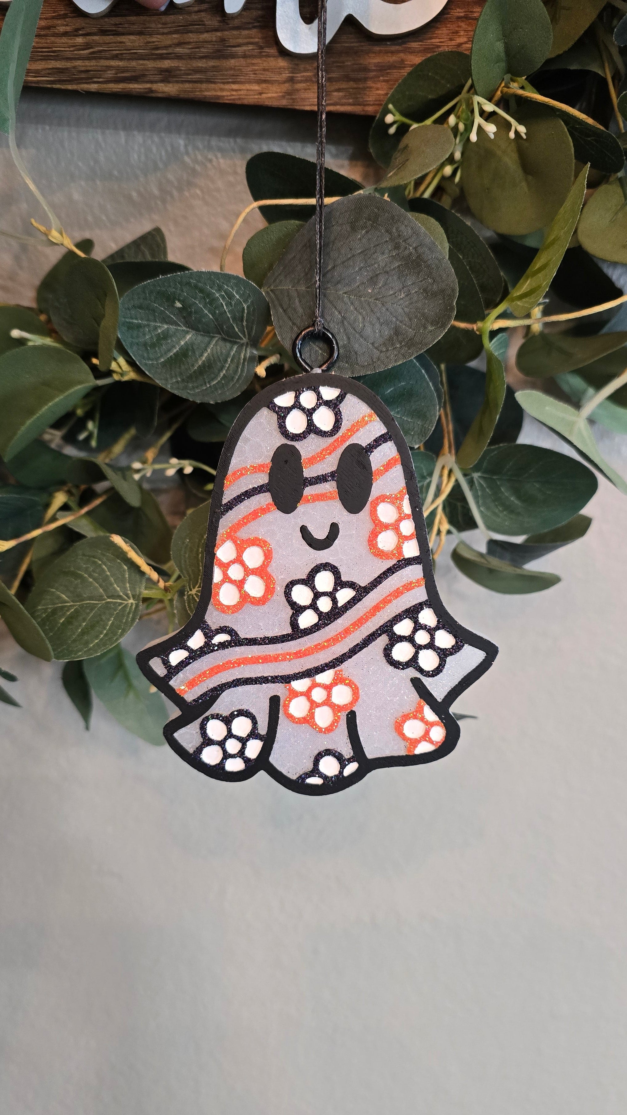 Handmade ghost-shaped car freshie with orange and black floral accents and a smiling face hanging from a rearview mirror.