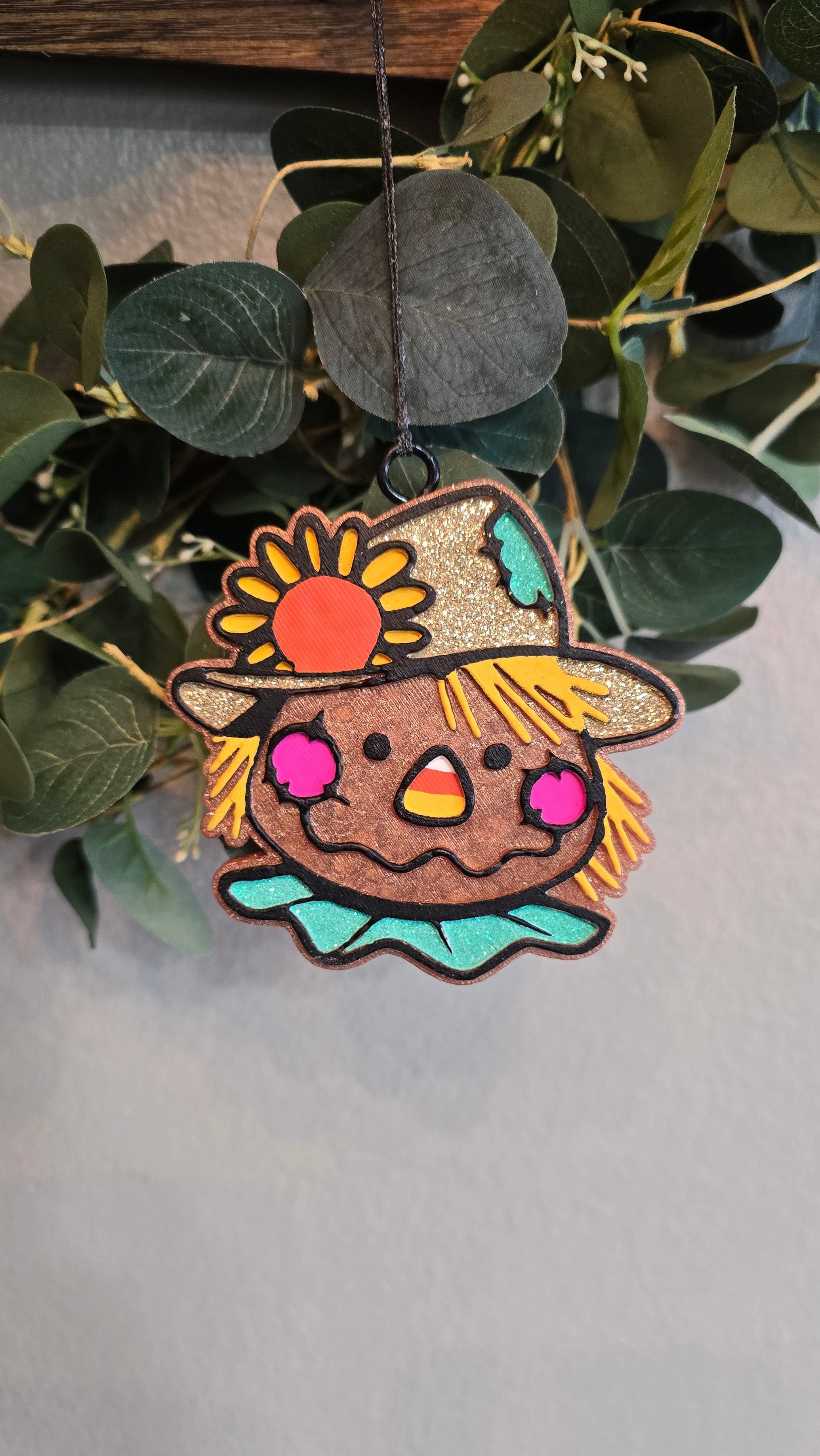 Handmade scarecrow car freshie with a sunflower on its straw hat, rosy cheeks, and bright autumn colors, hanging from a rearview mirror.